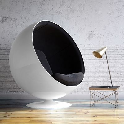  Eero Aarnio - Chaise Ball noire et blanche dans une pi&egrave;ce avec un parquet en bois et un fond gris. A droite de la chaise se trouve une table basse avec une lampe pos&eacute;e dessus.